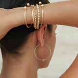 Close-up of a person wearing gold hoop earrings and bracelets on a neutral background