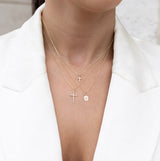 Woman wearing a trio of 14kt gold and diamond crosses in a white blazer.